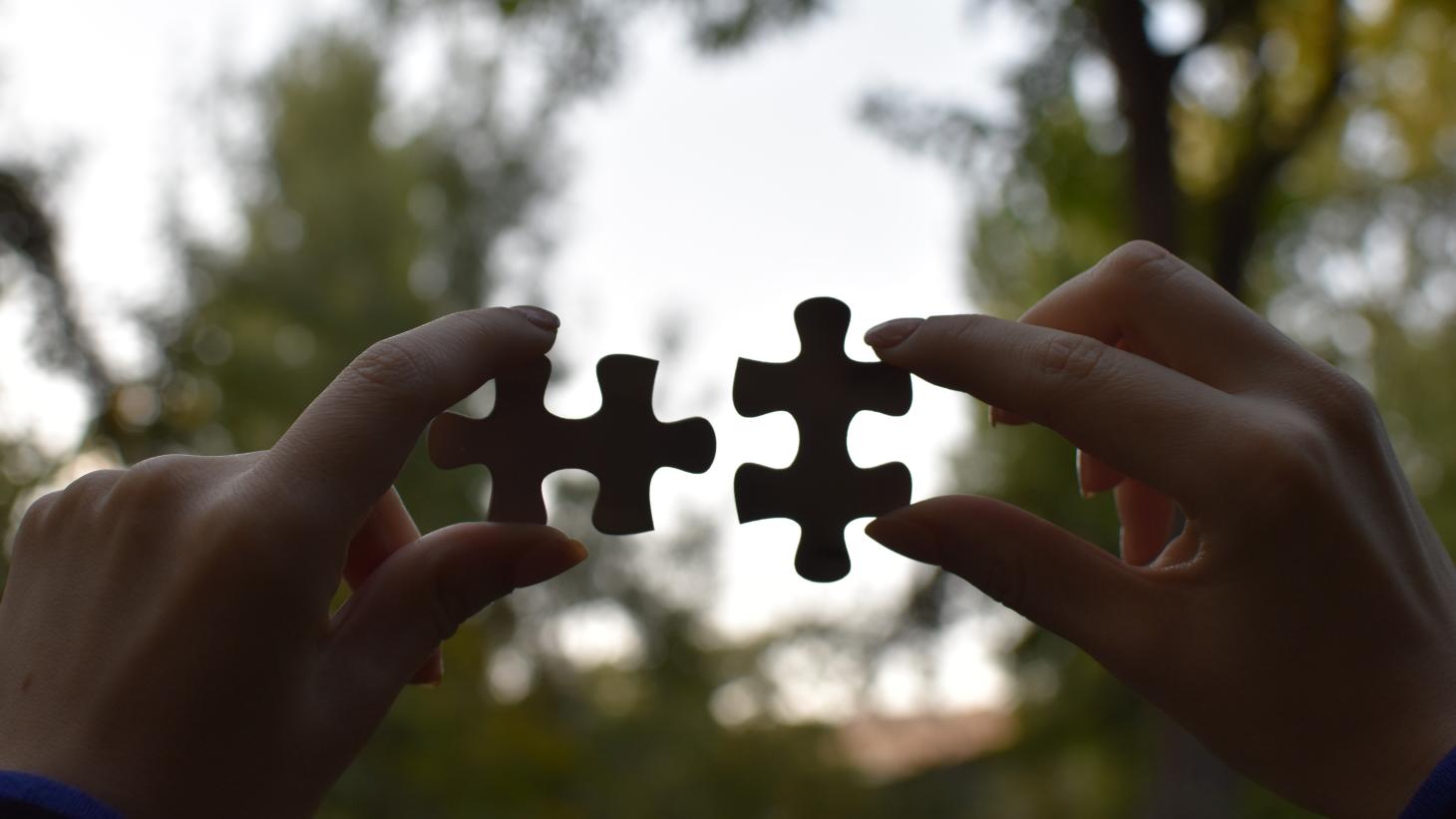 two hands holding up two jigsaw pieces that would fit together