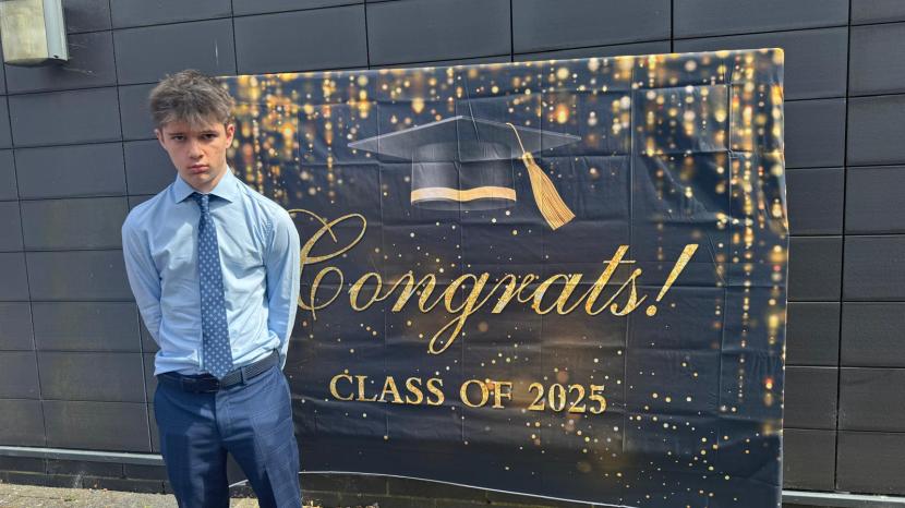 Jake standing in front of a graduation banner