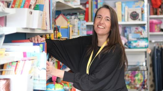 Volunteer filling shelves and smiling in charity shop