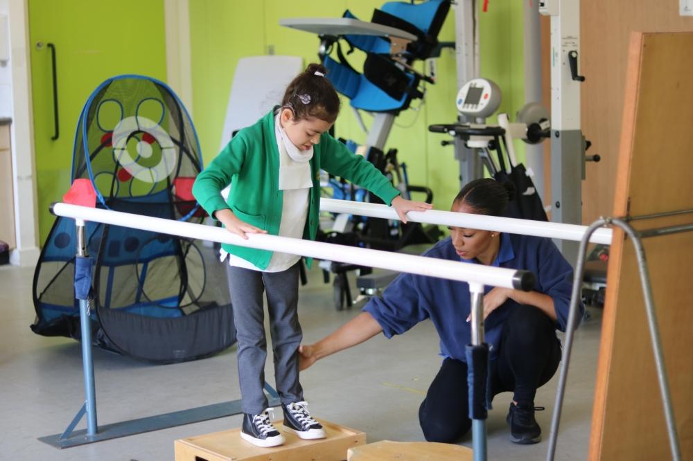 Shakeerah walking using bars and assisted by her physiotherapist