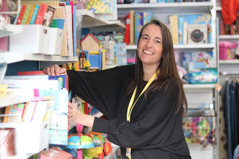 Volunteer filling shelves and smiling in charity shop