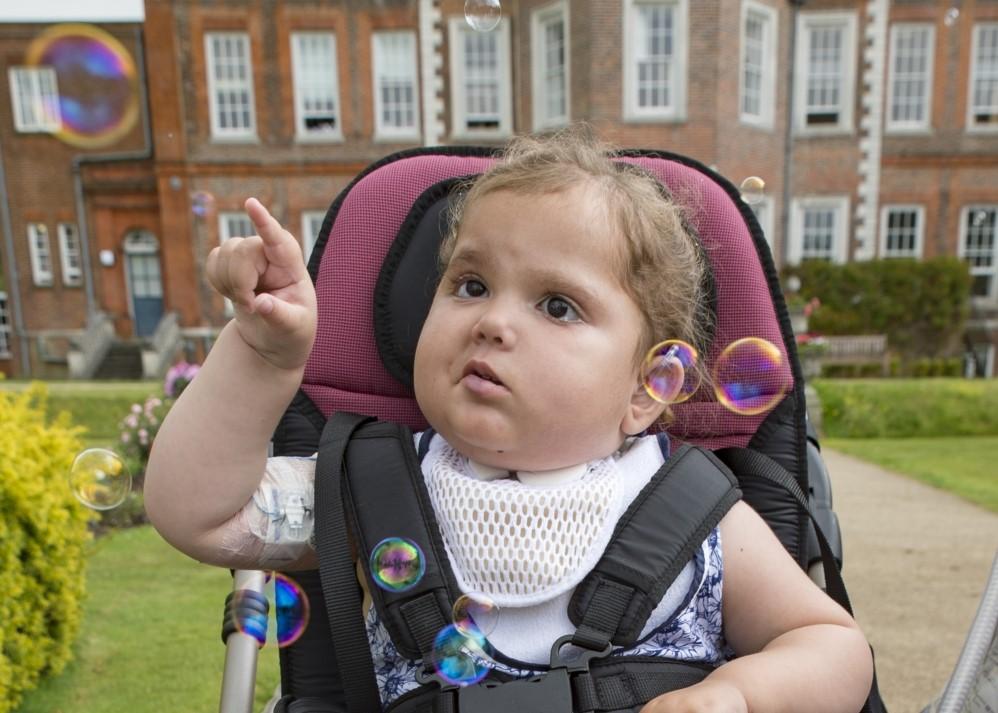 A little girl sitting in a wheelchair popping bubbles with her finger