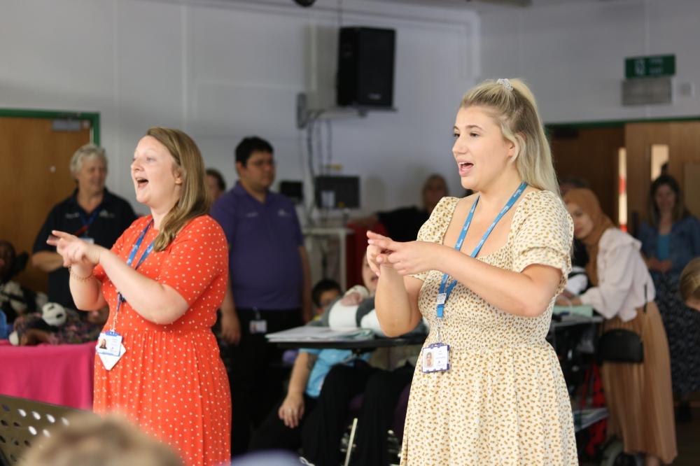 Two people standing in front of an audience singing and signing.