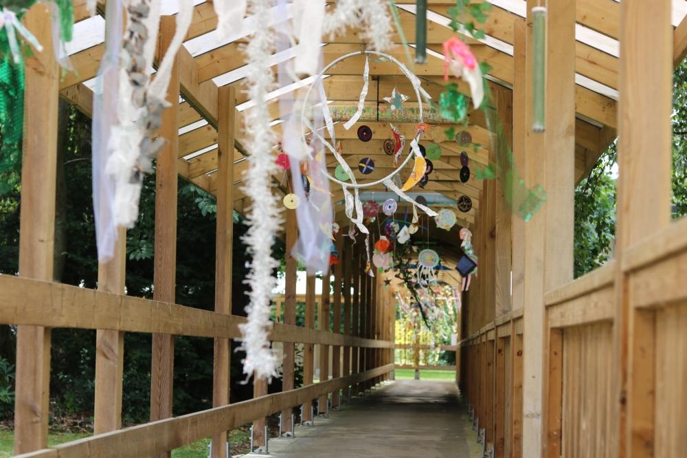Objects made from different materials hang from a wooden walkway.