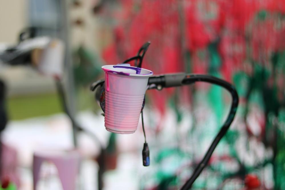 A cup filled with paint attached to the arm of a mechanism