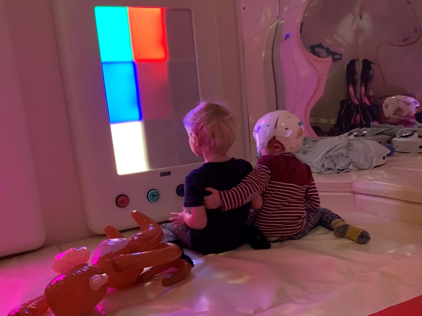 Millie in a soft play sensory room with her arm around her brother