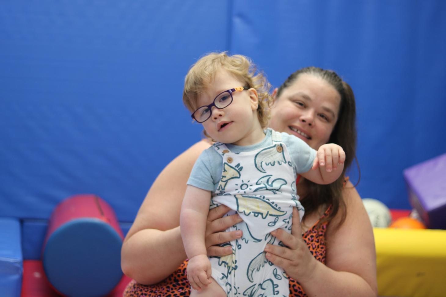 Teddie standing in a soft play room, his mum supporting him from behind.