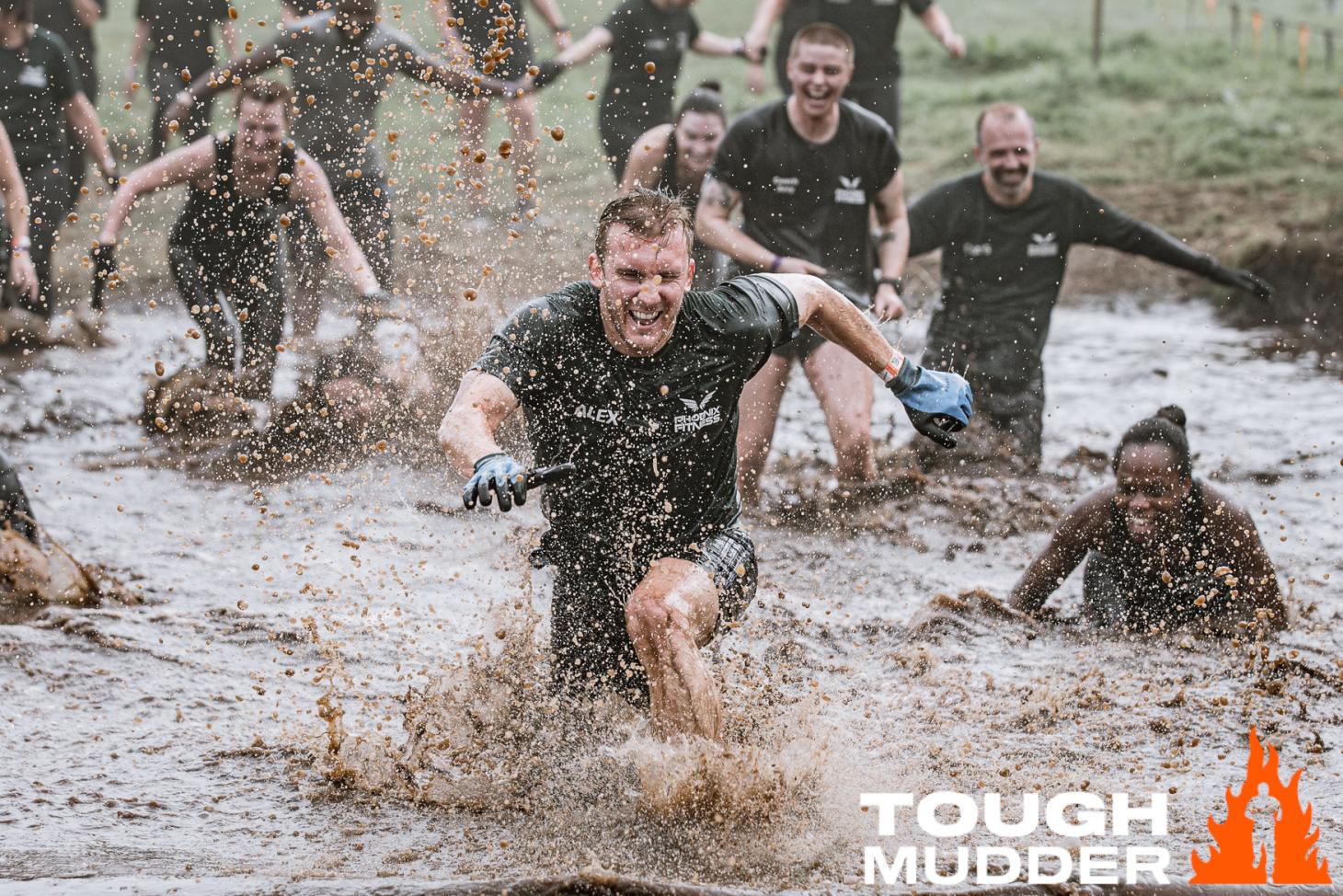 smiling man splashing through a muddy pool of water with fellow racers falling behind him
