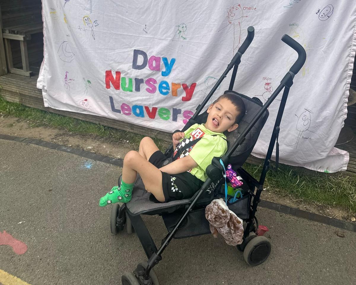 Seb in a pushchair in front of a sign that says Day Nursery Leavers