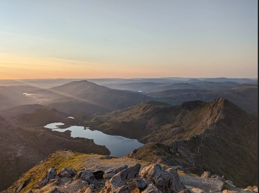 Beautiful sunrise sky ranging from blue to orange, overlooking the welsh valley from high up in Snowdonia, with breathtaking beauty of the lake and rocks below