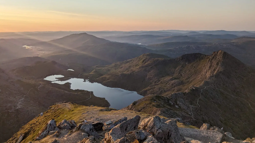 Beautiful sunrise sky ranging from blue to orange, overlooking the welsh valley from high up in Snowdonia, with breathtaking beauty of the lake and rocks below