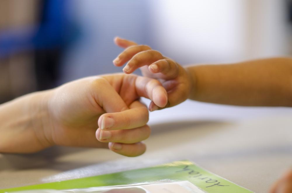 A small child's hand reaching out to hold an adult's finger