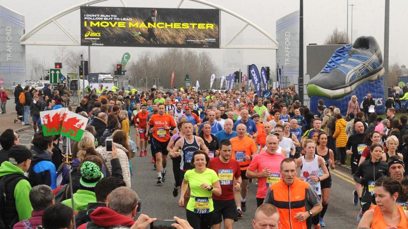 runners in high visibility coloured clothing under a black and yellow i love Manchester banner with a grey inflatable trainer to the right